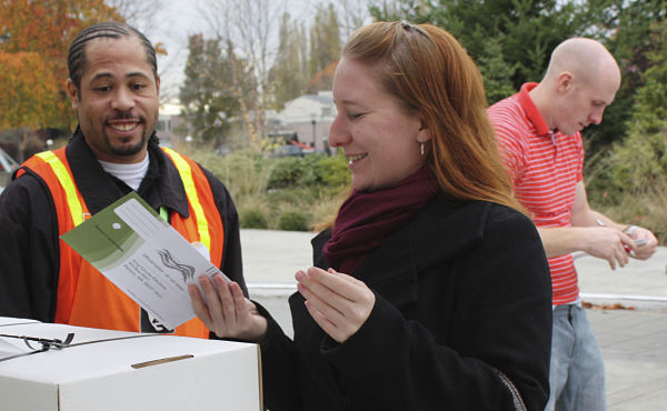 General-election volunteer Ryan Howlett II of Seattle watches as Nicole Bowman of Woodinville submits her ballot this afternoon at a Redmond City Hall dropbox. The dropboxes — one for walk-up voters and one for drive-up voters — will be open until 8 p.m. tonight.