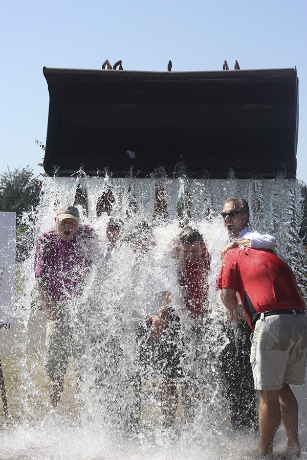 A group of six men upped the ALS Ice Bucket Challenge ante and are doused with ice and water from a backhoe at The Golf Club at Redmond Ridge today. They are Steve Barker