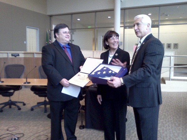 City of Redmond Mayor John Marchione (left) is presented with a certificate and U.S. flag by U.S. Reps. Suzan DelBene and Dave Reichert.