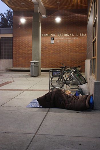 A homeless person rests at one of the entrances of the Redmond Regional Library  on Wednesday morning.